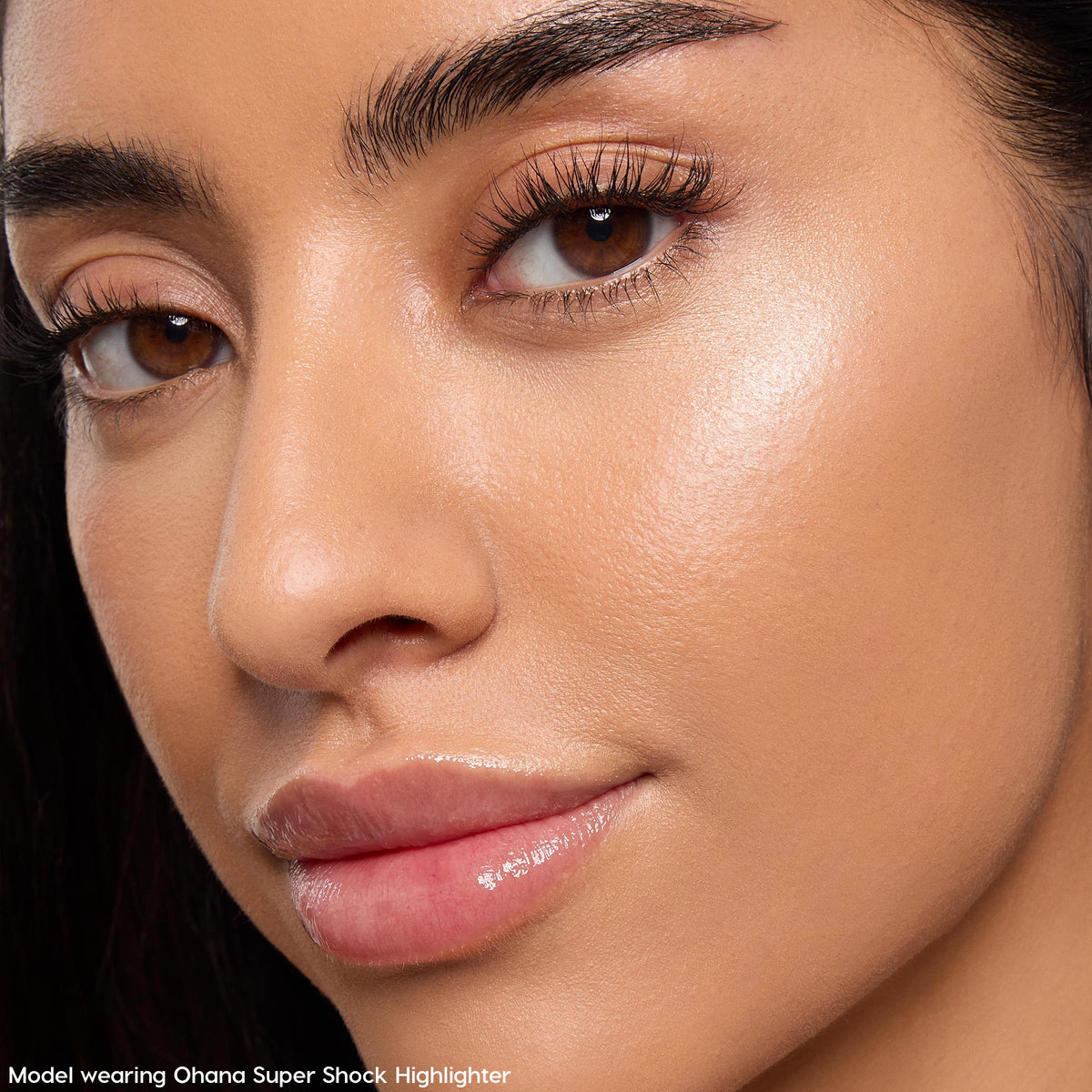 Model wearing Ohana Super Shock Highlighter, showing a luminous champagne glow on the cheekbone with defined brows and glossy lips in a tight face crop; part of the Disney Lilo & Stitch Collection, ColourPop Full Collection Set.