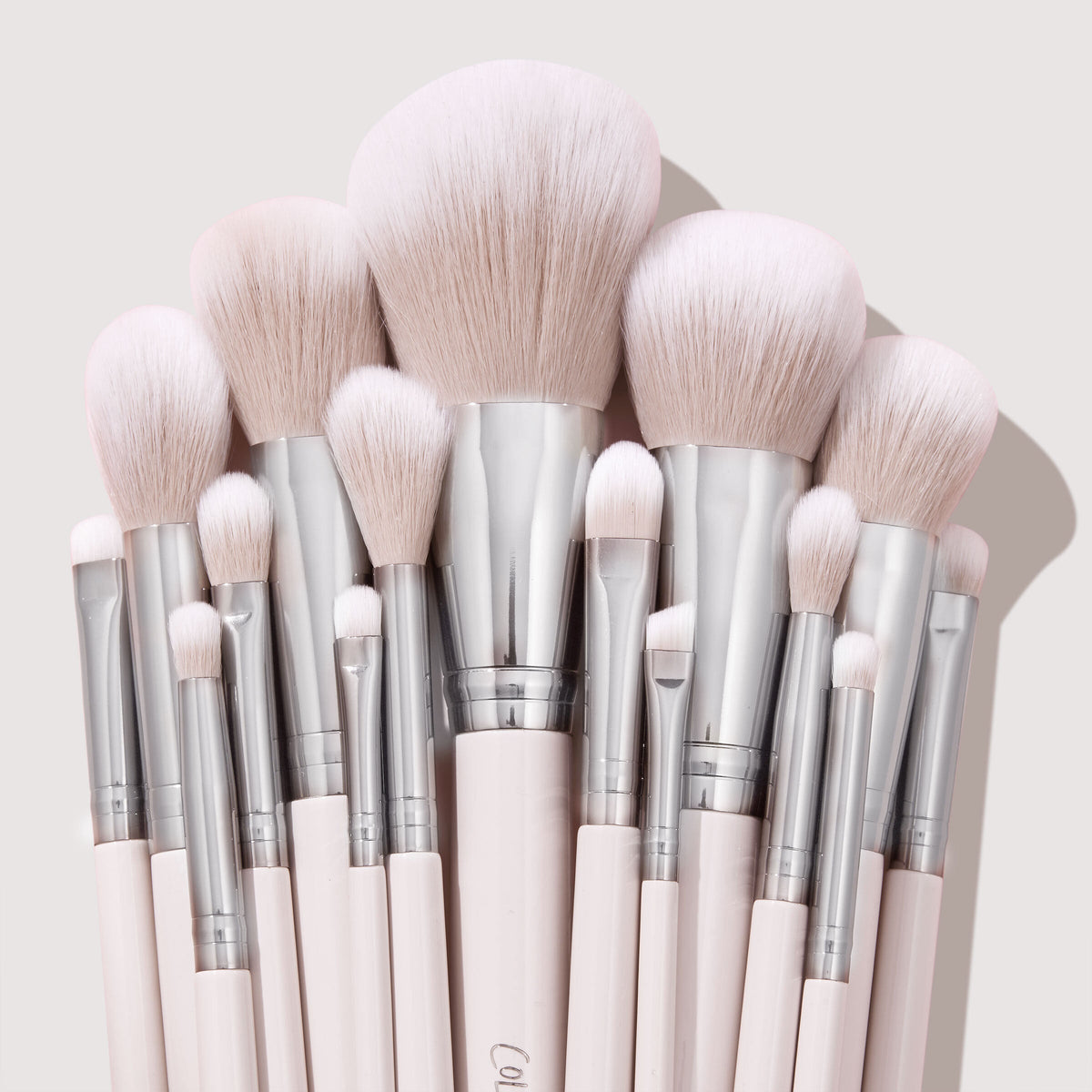 Stone Cold ColourPop Makeup Brush Kit fanned upright, displaying powder, blush, contour, and eye brushes with fluffy blush-pink bristles, silver ferrules, and pale pink handles, stacked tightly against a soft beige backdrop.