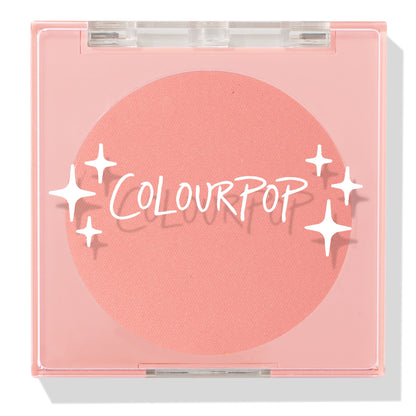 Swirled ColourPop Pressed Powder Blush compact closed, showcasing a warm peach‑coral matte pan beneath a clear pink lid with white starburst logo, square plastic case centered on a white background.