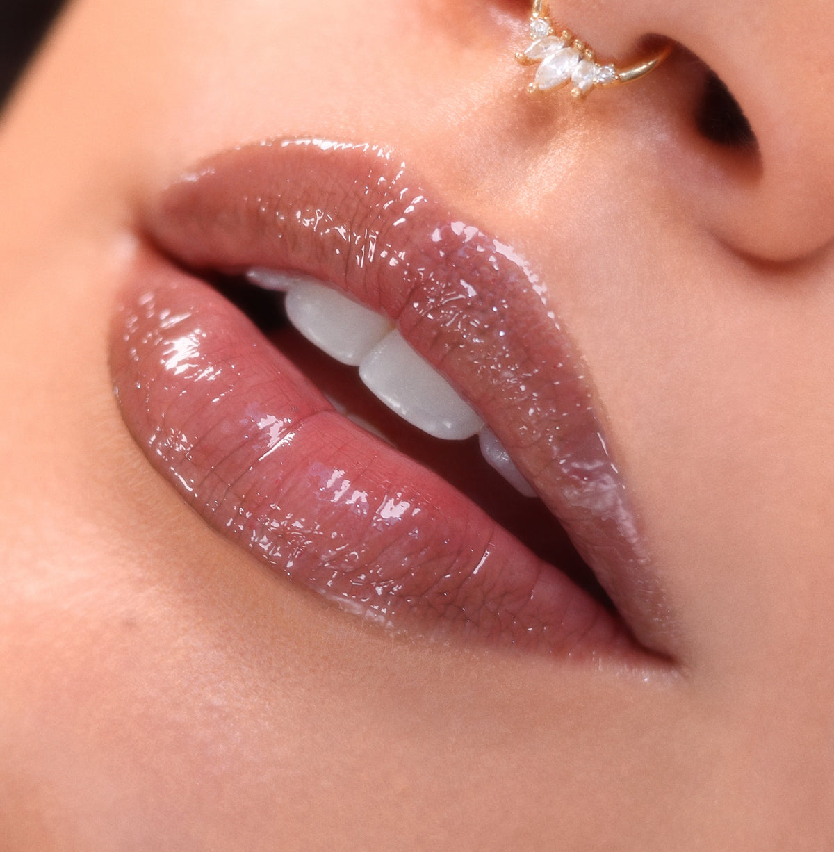 Glossy, plump lips wearing Vampy Lips Lux Lip Oil with a sheer pink-brown shine, teeth slightly parted; tight beauty close-up beneath a gold nose ring, showcasing the smooth, high-shine finish of ColourPop Lux Lip Oil.