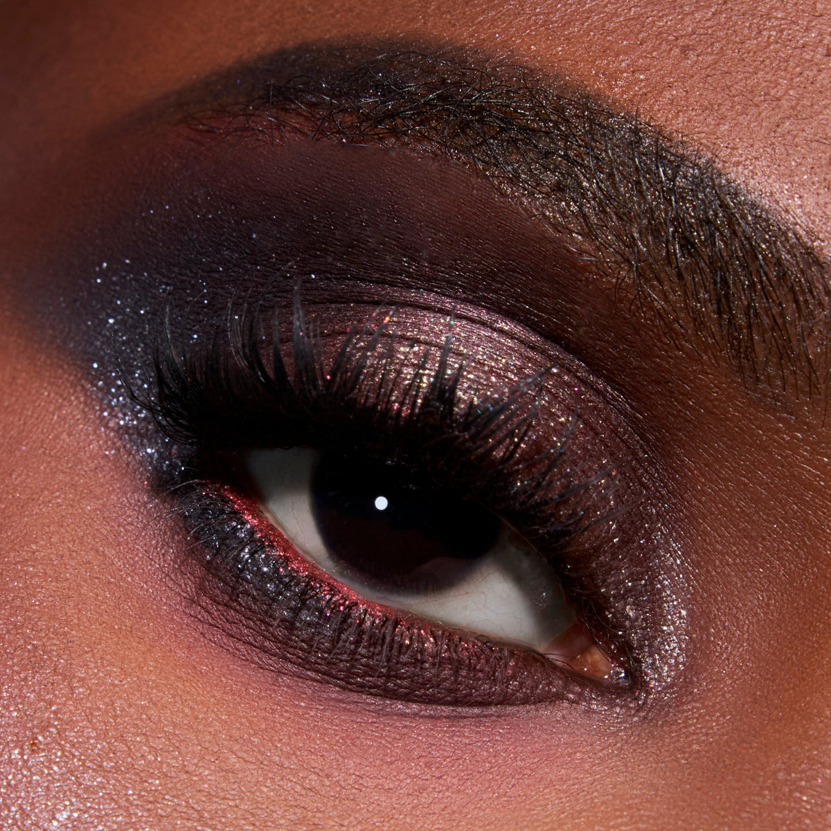Close-up eye wearing the Eternal Eclipse Eye Trio, showcasing shimmery Twilight-inspired smokey plum and charcoal shadow with metallic sparkle on the lid and lower lash line for a dramatic evening makeup look.