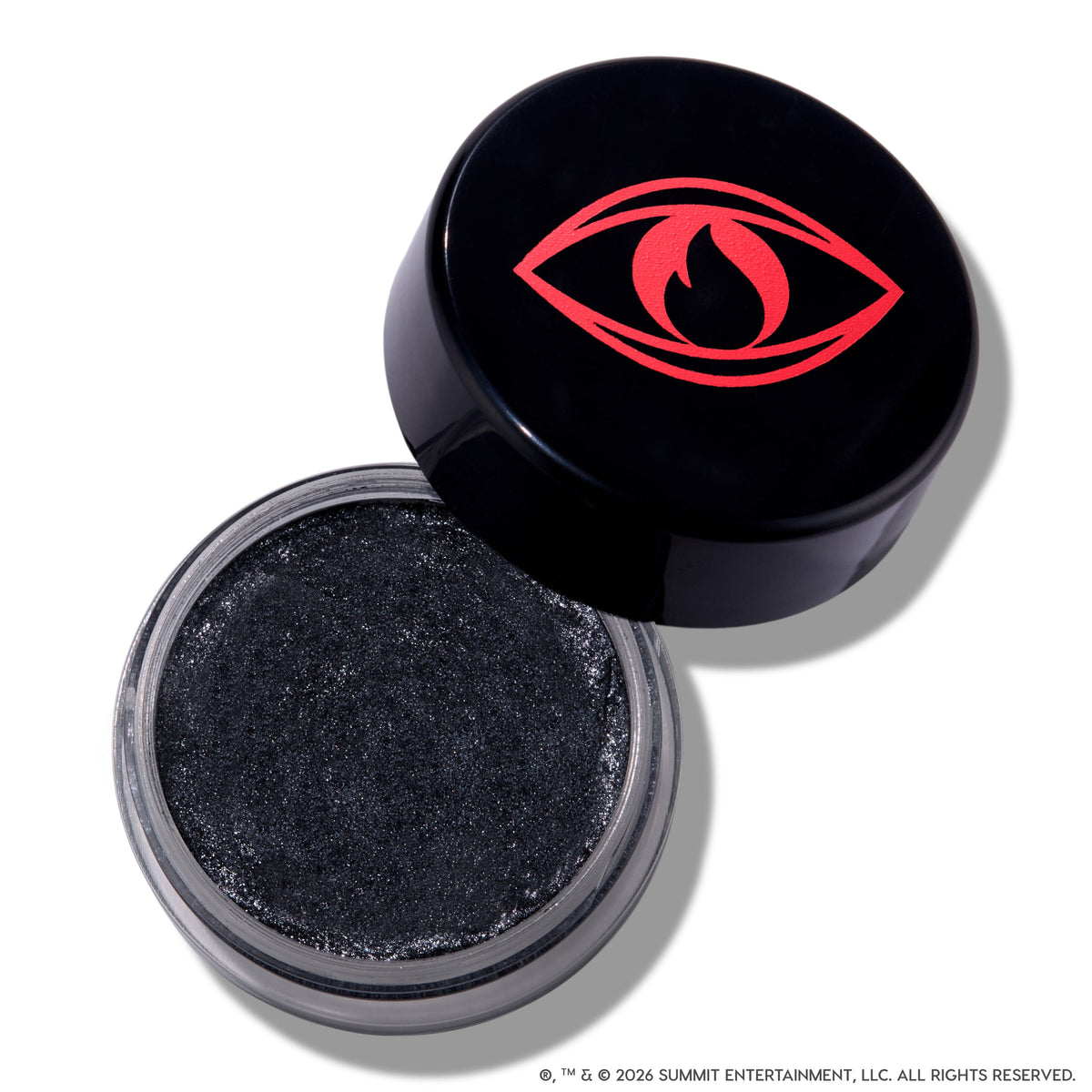 Open pot of ColourPop Newborn Army Jelly Much Shadow showing deep charcoal black, shimmer-packed cream eyeshadow, with the Twilight-inspired black lid featuring a bold red eye and flame icon resting beside it on a white background.