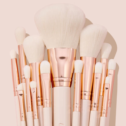 Ultimate Brush Roll, a ColourPop Makeup Brush Kit, fanned upright with soft white bristles, rose-gold ferrules, and cream handles, showcasing face and eye brushes for powder, blush, and eyeshadow blending on a blush-pink studio backdrop.