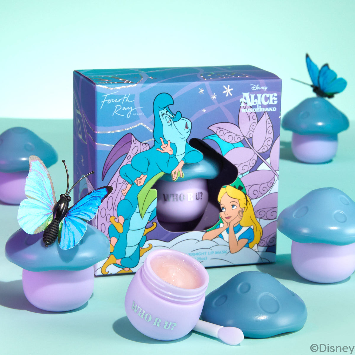 Pure Madness lip mask presenting an open lavender jar of glossy pink balm with spatula, surrounded by mushroom-shaped pots and a Disney Alice in Wonderland box with butterflies on a mint backdrop; a fun, giftable ColourPop Lip Mask.