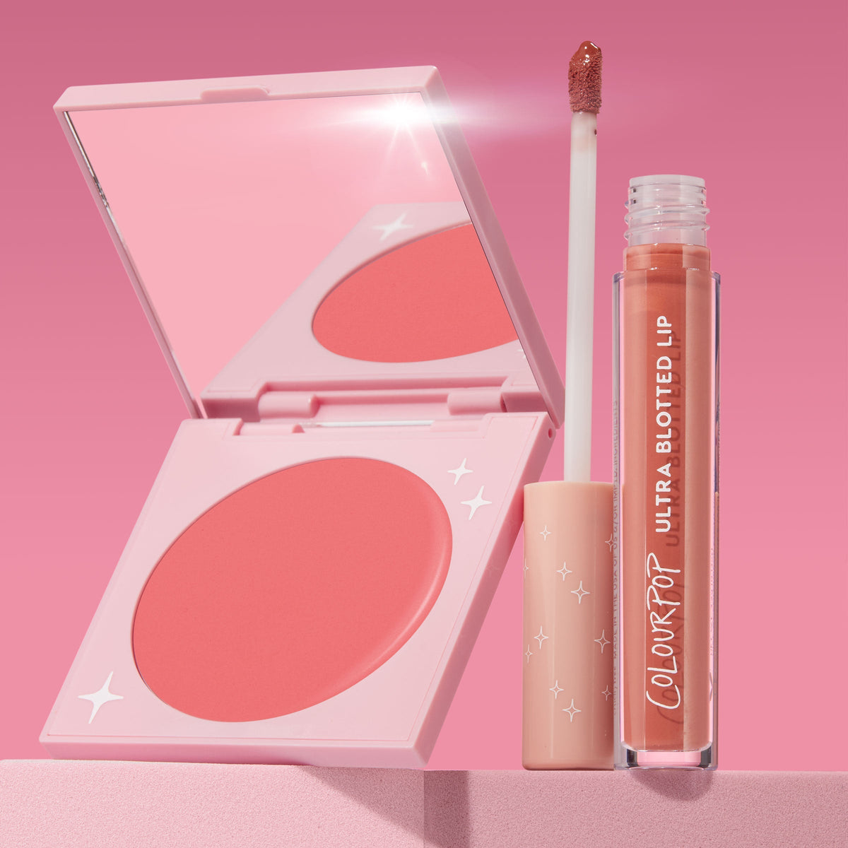 Mood 24/7 ColourPop Cheek & Lip Set showcasing an open pink compact of coral blush with mirror and star accents beside an Ultra Blotted Lip tube with doe-foot applicator, standing on a soft pink pedestal against a gradient pink backdrop.