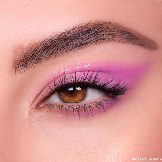 Brown eye wears In The Clear Face & Eye Gloss, creating a glassy wet-look over pink‑lavender shadow; fluttery lashes and a defined brow frame the lid, showcasing ColourPop Face & Eye Gloss shine in a macro beauty close-up.