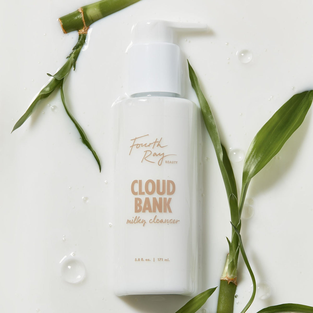 Cloud Bank Milky Cleanser bottle by Fourth Ray Beauty rests on a glossy, milk-like surface with water droplets, framed by green bamboo leaves; white pump-top 5.8 fl oz (171 ml) packaging, presented as a gentle ColourPop Face Cleanser.
