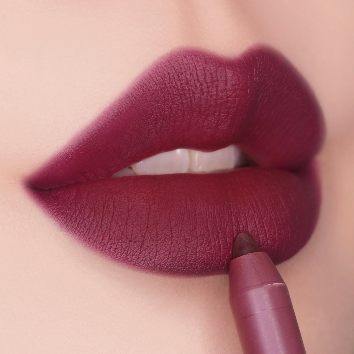 Berry-red matte lips being precisely lined with the ColourPop Lippie Pencil in On Ice, creamy tip tracing the lower lip for crisp definition, close-up studio shot highlighting smooth texture and rich, cool-toned plum color.